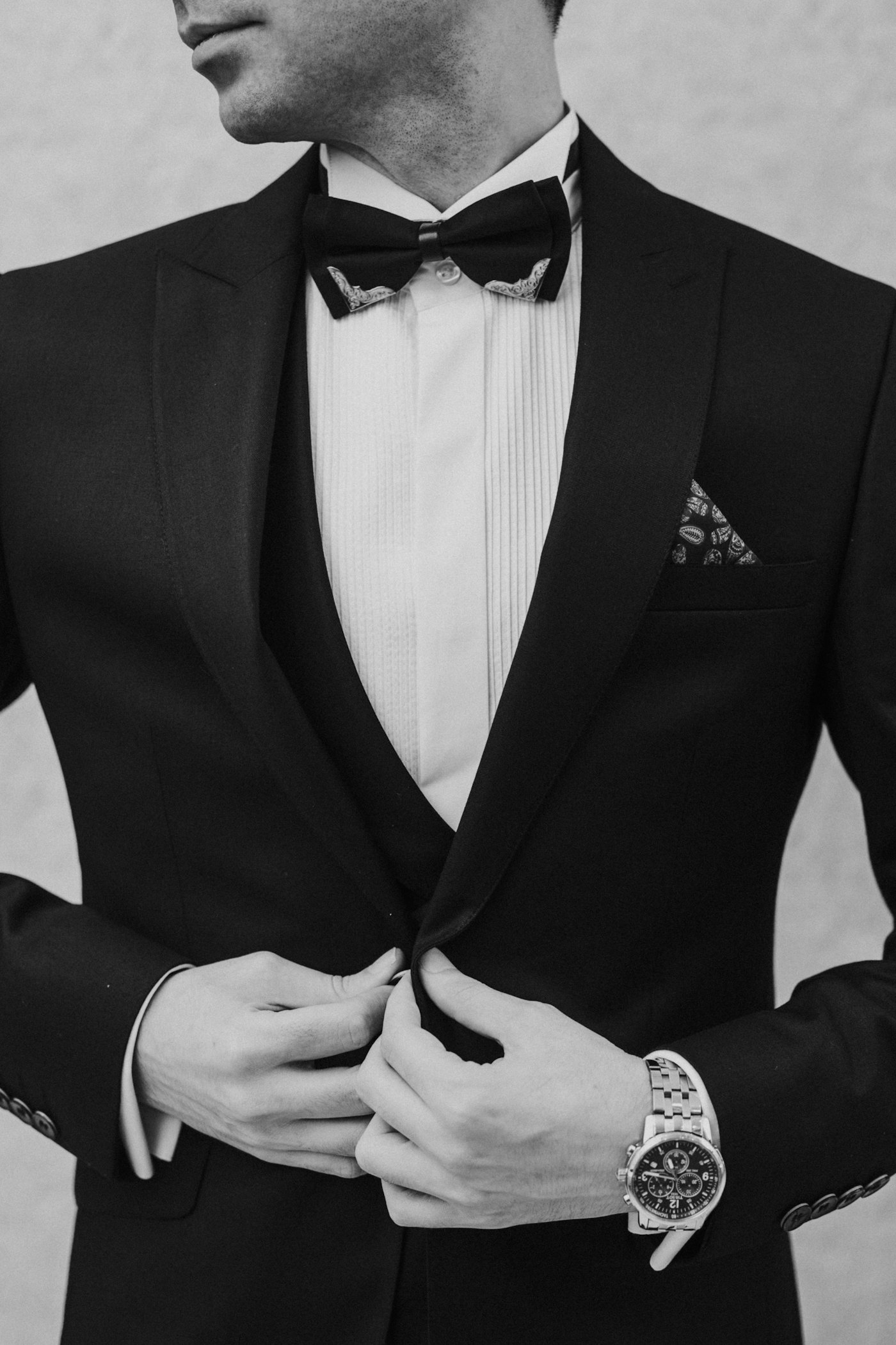 A man in a dinner jacket fastening his button, bow tie and pocket square